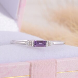 May include: A delicate silver ring with a rectangular amethyst gemstone and two smaller diamond accents.