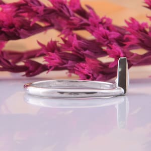 May include: A silver ring with a simple, sleek design. The band is thin and the ring has a slightly pointed edge.