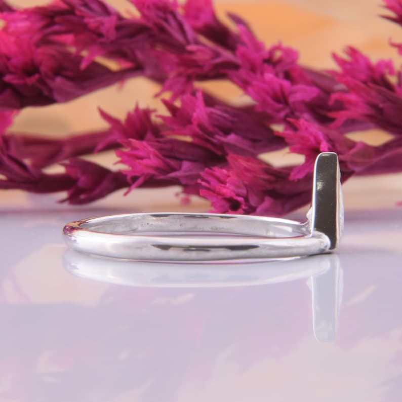 May include: A silver ring with a simple, sleek design. The band is thin and the ring has a slightly pointed edge.