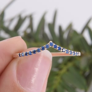 May include: A gold band ring with a chevron shape set with small blue sapphires.