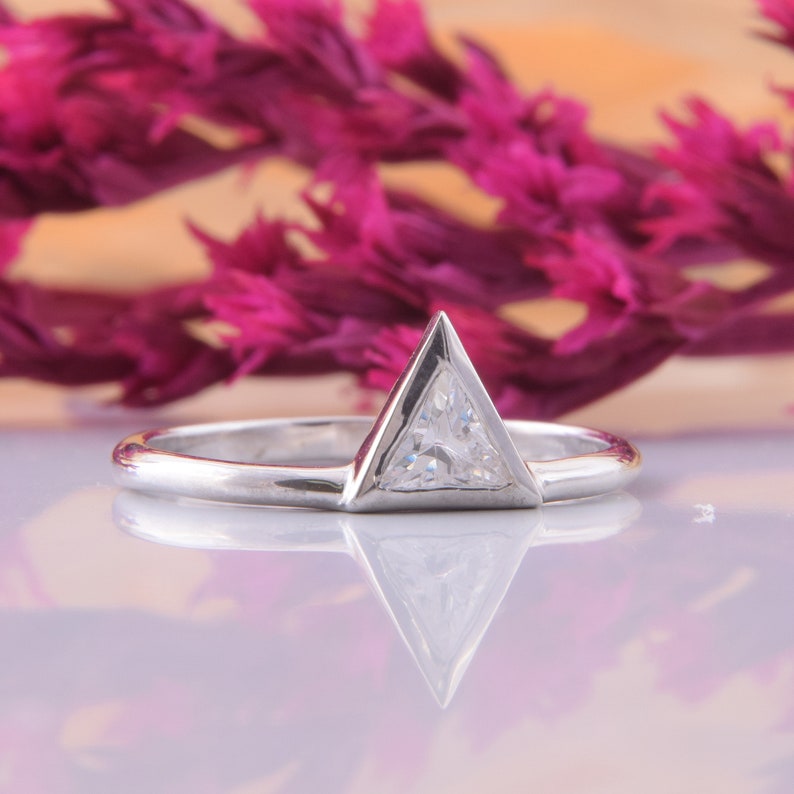 May include: A silver ring with a triangular shaped diamond set in a prong setting.