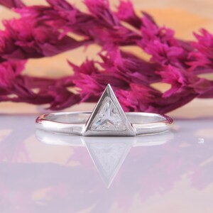 May include: A silver ring with a triangular shaped clear gemstone set in the center.