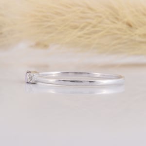 May include: A delicate silver band ring with a small purple gemstone and two tiny clear gemstones.