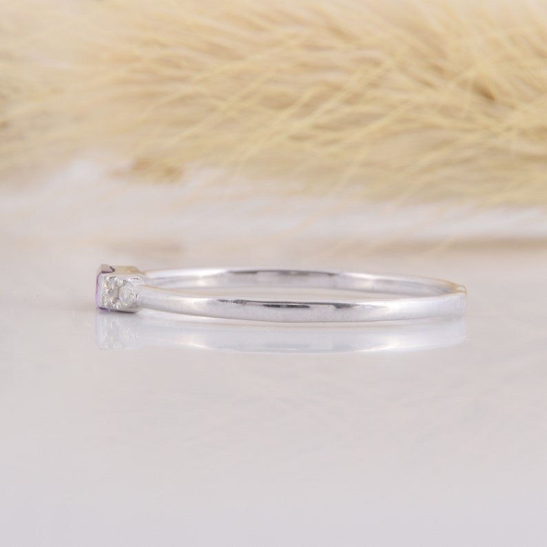 May include: A delicate silver band ring with a small purple gemstone and two tiny clear gemstones.