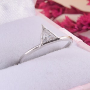 May include: A silver ring with a triangular shaped diamond set in the center. The ring is in a white box.