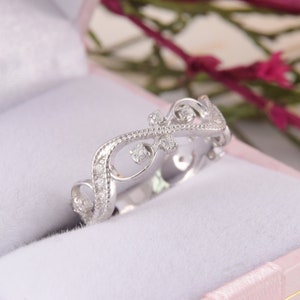 May include: A delicate silver ring with a floral design and small diamonds. The ring is in a white box with a pink lining.