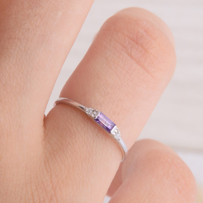 May include: A delicate silver ring with a small rectangular amethyst gemstone and tiny clear accent stones.
