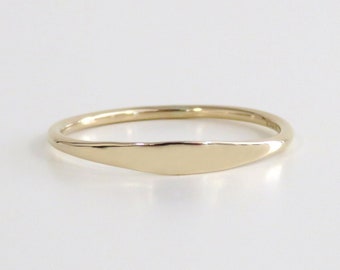 May include: A simple gold band ring with a flat, oval-shaped top.