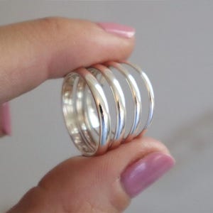 May include: A silver ring with a ribbed design. The ring has a wide band with multiple parallel grooves, creating a textured surface. The ring is held between fingers, showcasing its polished, reflective surface. The ring's design is simple yet elegant.