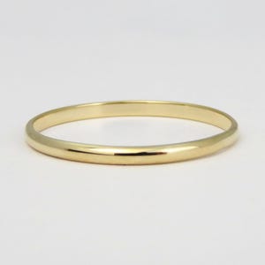Peut inclure: Un bracelet jonc de couleur or. Le bracelet rond et poli est une bande d'or massif. Le bijou est présenté sur un fond blanc. Ce bracelet simple et élégant convient à un usage quotidien.