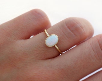 May include: A delicate gold ring with a white oval opal gemstone. The ring is simple and elegant, perfect for everyday wear.
