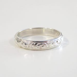 May include: A silver band ring with an intricate floral design engraved around the entire band.