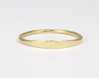 May include: A simple gold band ring with a flat, oval-shaped top.
