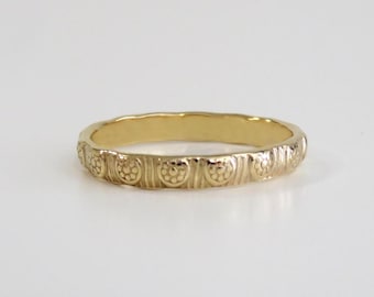 May include: A gold band ring with a textured design. The band is decorated with a repeating pattern of small circles.
