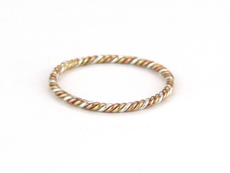 May include: A thin, twisted ring made of silver, gold, and rose gold.