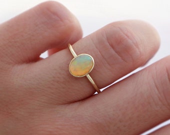 May include: A delicate gold ring with a light orange oval opal gemstone. The ring is simple and elegant, perfect for everyday wear.
