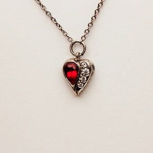 Może przedstawiać: Srebrny naszyjnik z serduszkowym wisiorem ozdobionym czerwonym kamieniem i przezroczystymi cyrkoniami.