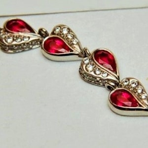Może przedstawiać: Trzy srebrne zawieszki w kształcie serca z czerwonymi kamieniami szlachetnymi i przezroczystymi akcentami kryształowymi.