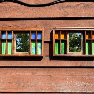 May include: Two rectangular wooden wall mirrors featuring integrated shelving compartments. The left mirror includes blue and green stained glass accents, while the right mirror features orange and green stained glass panels. Both frames are made of dark wood.