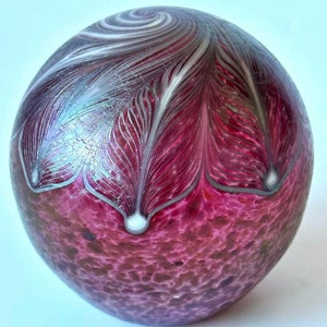 Può includere: Un fermacarte in vetro rosa con un design a spirale iridescente bianco e argento. Il fermacarte ha una superficie testurizzata.