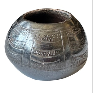 Puede incluir: Una olla de cerámica negra con forma redondeada y diseños geométricos intrincados tallados en la superficie.