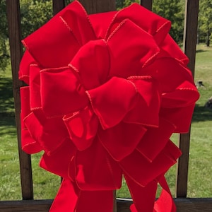 May include: A large, bright red velvet bow with a satin finish. The bow is tied with a long tail and has a decorative, stitched edge.