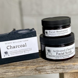 May include: A black charcoal goat milk soap bar and two jars of skincare products. The soap is labeled "Charcoal" and weighs 5 oz. The jars are labeled "Facial Moisturizer" and "Activated Charcoal Facial Scrub".
