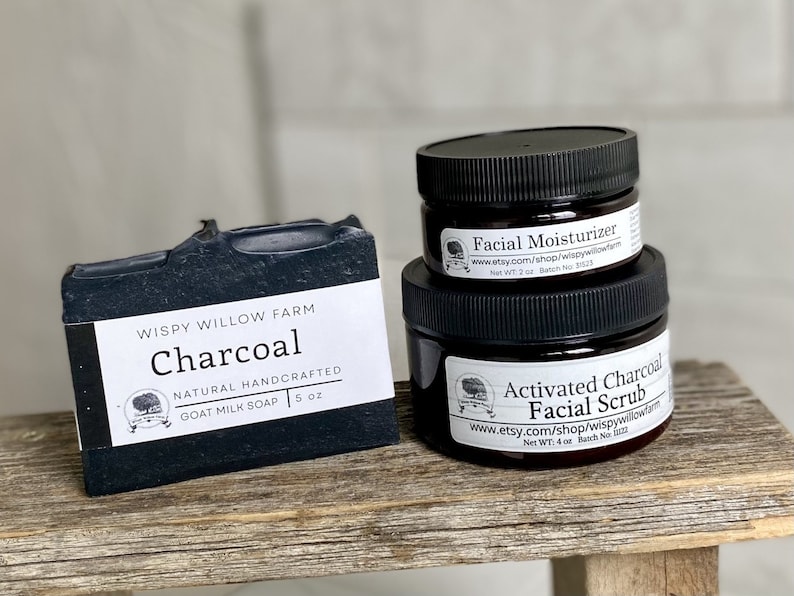 May include: A black charcoal goat milk soap bar and two jars of skincare products. The soap is labeled "Charcoal" and weighs 5 oz. The jars are labeled "Facial Moisturizer" and "Activated Charcoal Facial Scrub".