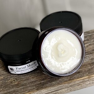 May include: Three small jars of facial moisturizer with black lids. One jar is open, revealing a creamy white product. The jars are labeled "Facial MoistM" and "Net WT. 2 oz."