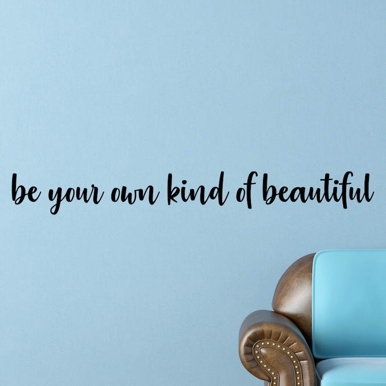 Pode incluir: Uma parede azul com o texto "be your own kind of beautiful" em letras cursivas pretas. Um sof&aacute; azul claro com encosto de couro marrom est&aacute; no canto inferior direito da imagem.