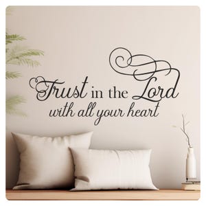 May include: A black and white wall decal with the text "Trust in the Lord with all your heart". The decal is on a white wall with a couch and pillows in front of it.