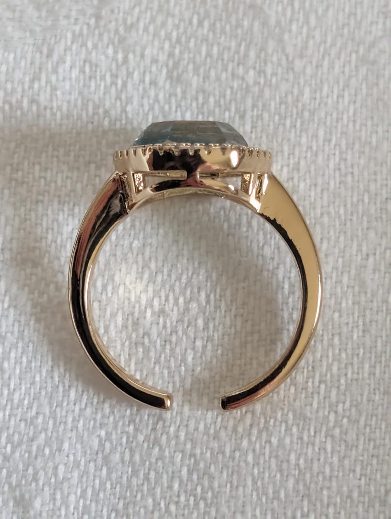 Pu&ograve; includere: Un anello color oro con una grande pietra preziosa azzurra. La pietra, di forma ovale, &egrave; incastonata in una montatura decorativa. Il gambo dell'anello &egrave; aperto in basso.