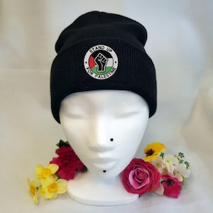 May include: Black beanie with a white embroidered patch that says "Stand Up For Palestine" with a raised fist and the Palestinian flag colors.