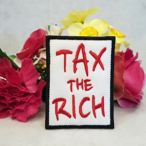 May include: White fabric patch with a black border and red embroidered text that reads "Tax the Rich".