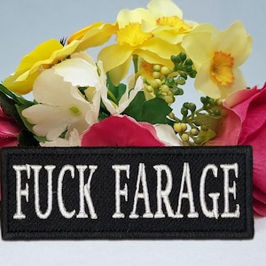 Puede incluir: Un parche rectangular negro con el texto blanco "FUCK FARAGE" se muestra frente a un arreglo floral. Las flores incluyen rosas rosas, amarillas y blancas.