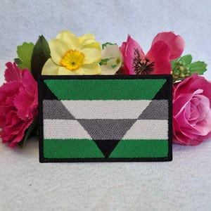May include: Green, white, and gray embroidered patch with a chevron design. The patch is surrounded by pink and yellow flowers.