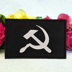 Könnte beinhalten: Ein schwarzer Stoff-Patch mit einem weißen gestickten Hammer-und-Sichel-Symbol.