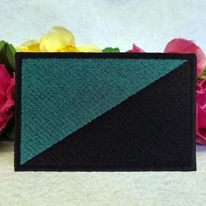 May include: A black and teal green embroidered patch with a diagonal line dividing the two colors. The patch is on a white background.