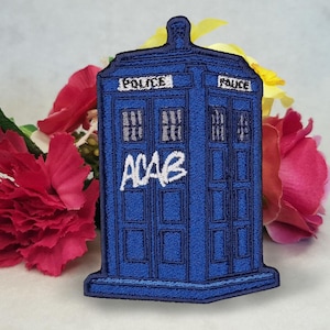 May include: Blue and black embroidered patch of a police box with the words "Police" on the side and "ACAB" written in white on the front.
