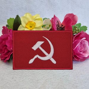 Könnte beinhalten: Roter Stoff-Patch mit einem weißen gestickten Hammer und Sichel.