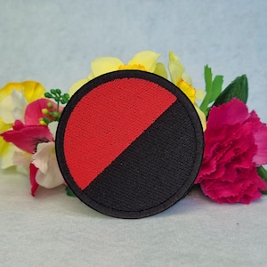 Peut inclure: Un écusson brodé noir et rouge avec un motif circulaire. La moitié du cercle est rouge et l'autre moitié est noire.