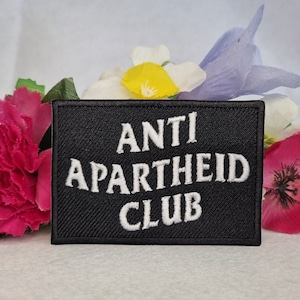 May include: Black embroidered patch with white text that reads "ANTI APARTHEID CLUB".