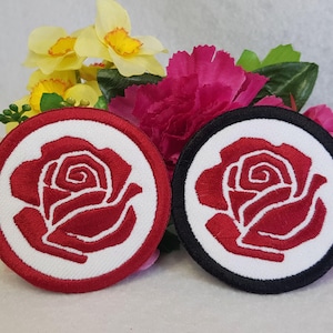 May include: Two embroidered iron-on patches featuring a red rose on a white background. One patch has a red border and the other has a black border.