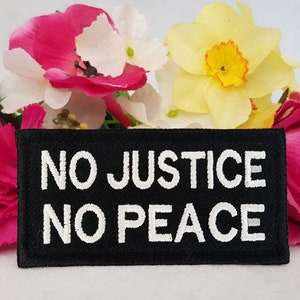Könnte beinhalten: Schwarzer gestickter Aufnäher mit weißem Text, der "NO JUSTICE NO PEACE" lautet. Der Aufnäher ist von rosa und gelben Blumen umgeben.