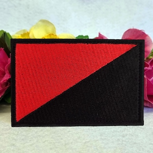 Op de afbeelding: Een rechthoekige geborduurde patch met een diagonaal verdeeld ontwerp. De linkerbovenhoek is felrood, terwijl de rechteronderhoek effen zwart is. De gehele patch is afgewerkt met een dikke, zwart gestikte rand voor een strakke uitstraling.