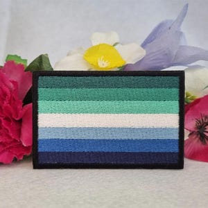 Può includere: Una toppa ricamata che rappresenta la bandiera del pride genderqueer. La toppa è verde, bianca e blu con un bordo nero.