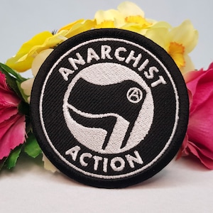 May include: A black and white embroidered patch with the text "ANARCHIST ACTION" in a circle around a stylized fist with an "A" in a circle inside it.