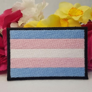 May include: A blue, pink, and white transgender pride flag patch with black stitching around the edges.