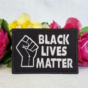 Op de afbeelding: Black Lives Matter patch met een opgeheven vuist in witte borduurwerk op een zwarte achtergrond.