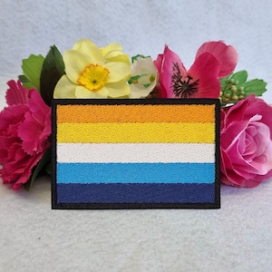 May include: A colourful embroidered patch with five horizontal stripes in orange, yellow, white, blue, and dark blue. The patch is surrounded by a black border.